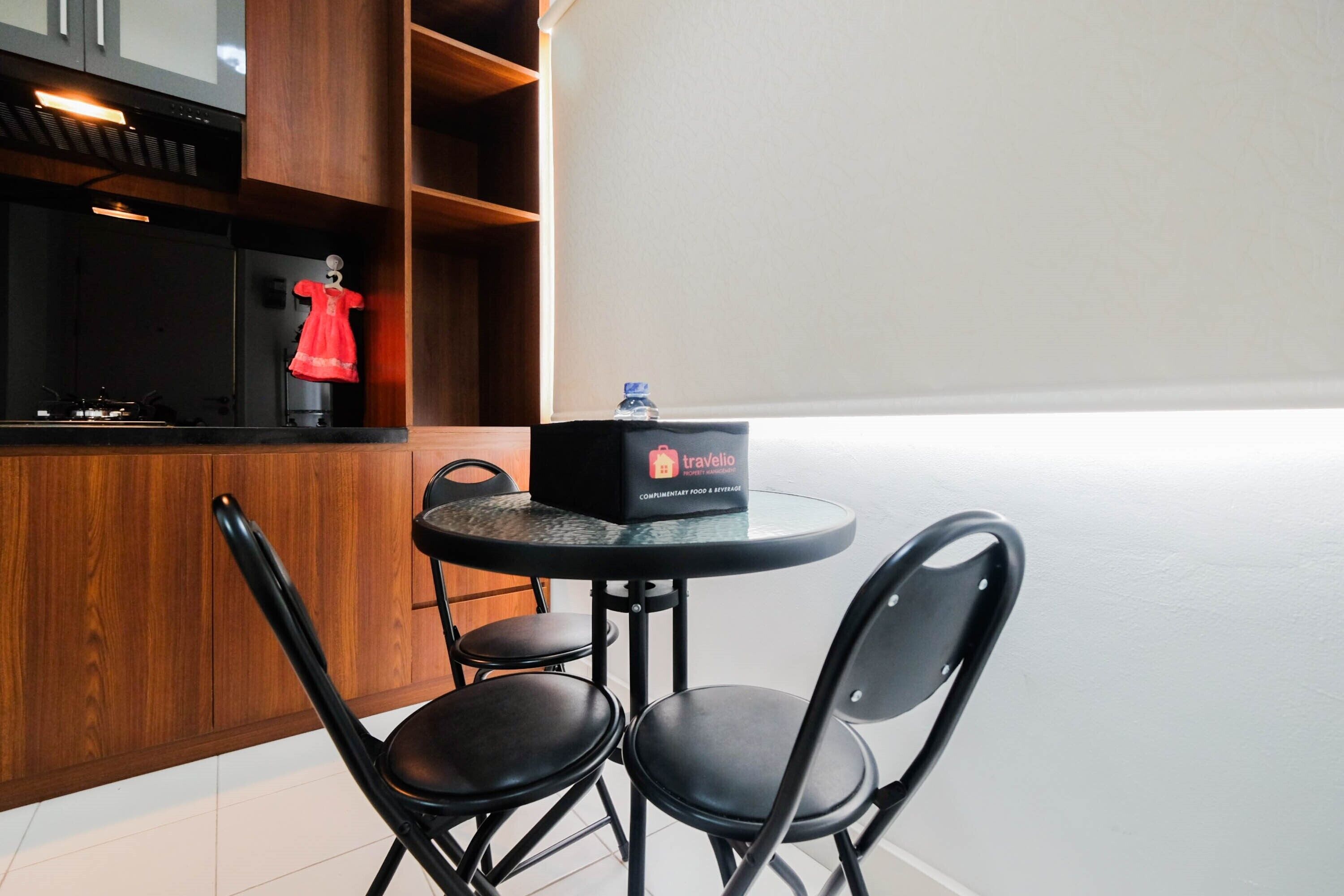 A compact kitchen area with a round table and four chairs, a water bottle on the table, and a red dress hanging on a rack.