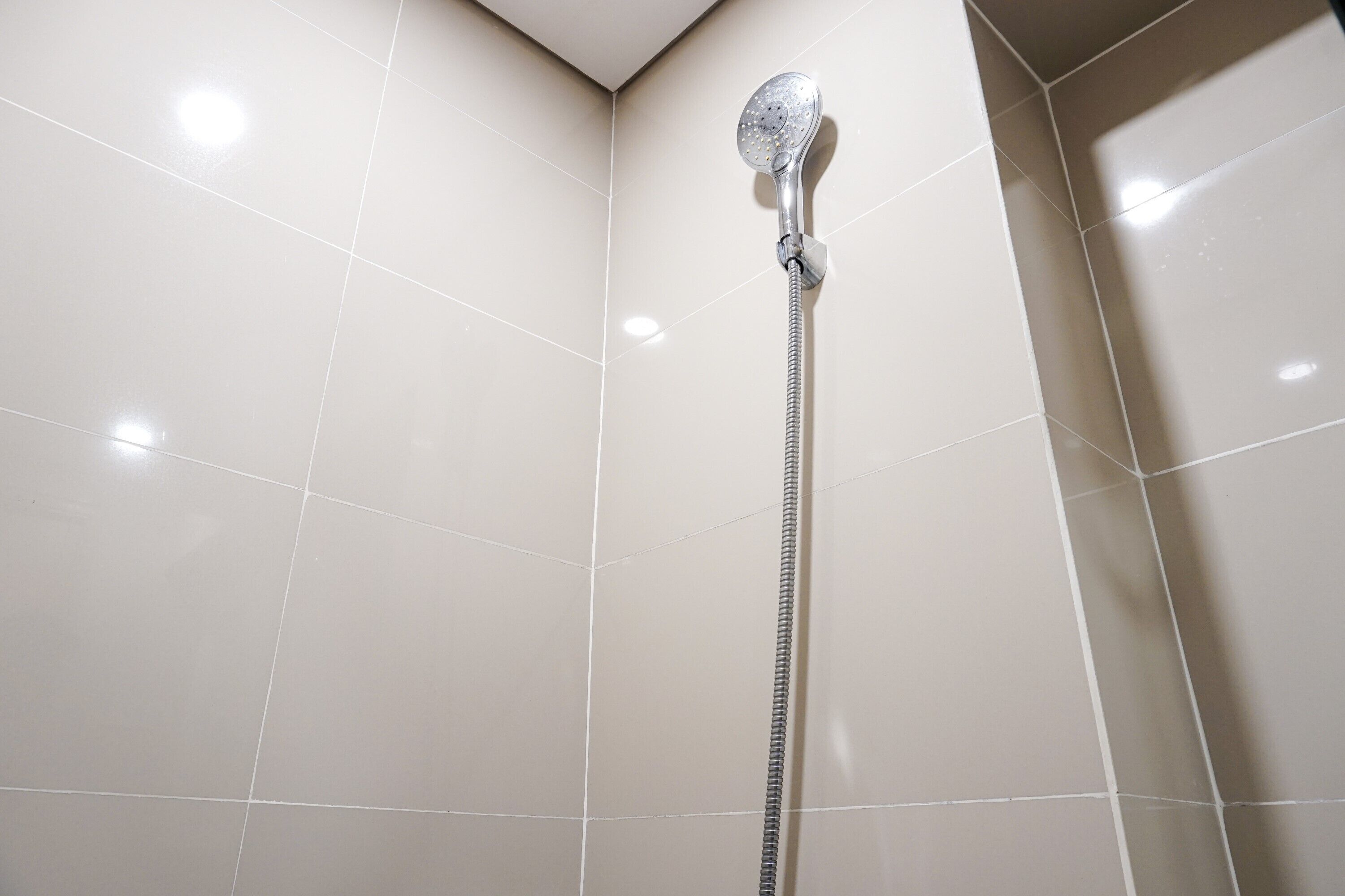 A shower area with a handheld showerhead and a flexible hose.