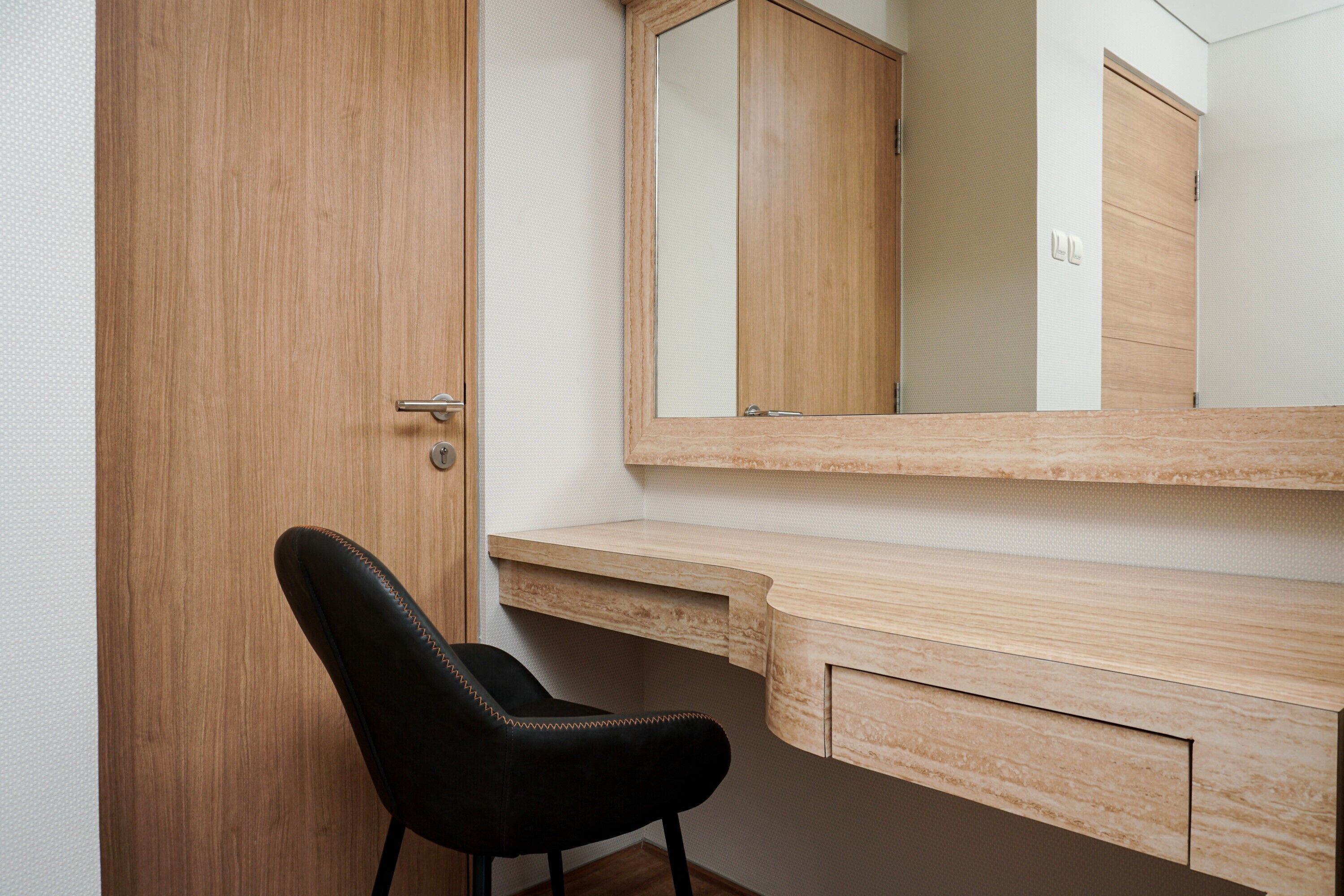 A wooden door, a black chair, a wooden desk, and a mirror.