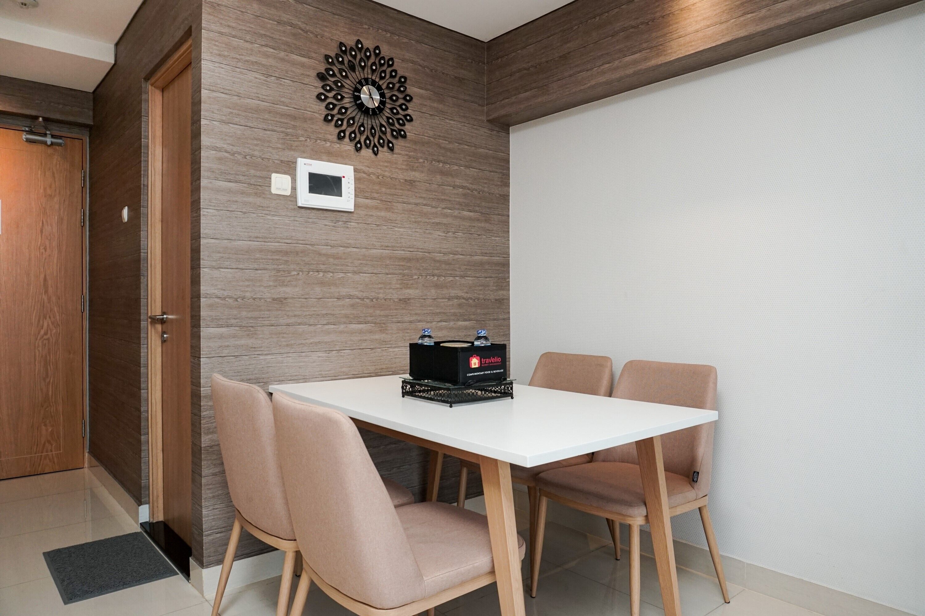 A modern dining area with a white table and four chairs, a decorative wall piece, and a minibar.