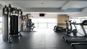 A gym with various exercise equipment including a treadmill, elliptical, and weight machines. - Stunning 2BR Loft Apartment at Maqna Residence (Jakarta)