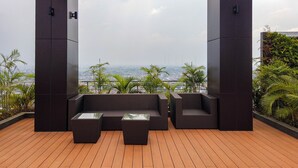A rooftop terrace with wicker furniture, a wooden floor, and a view of the cityscape. - Stunning 2BR Loft Apartment at Maqna Residence (Jakarta)