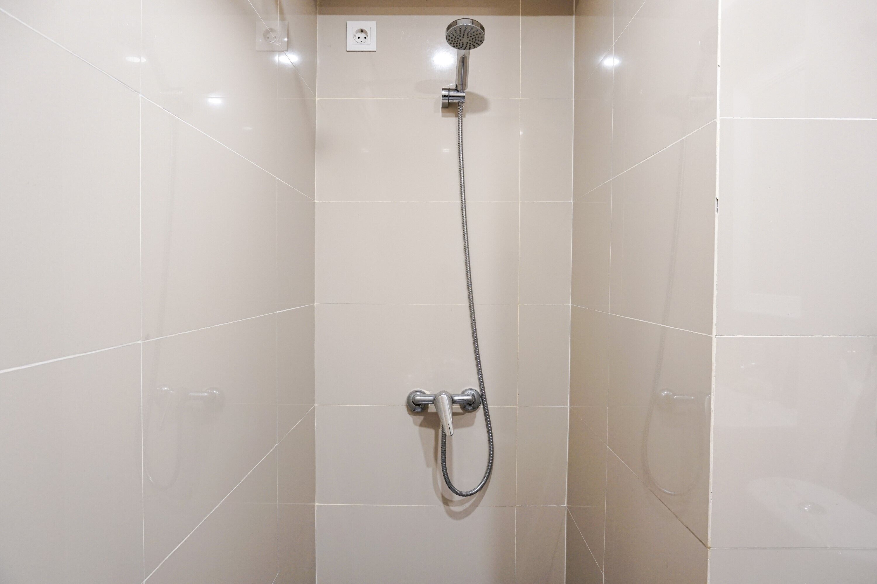 Une douche équipée d’un pommeau de douche à main et d’un pommeau de douche fixe, tous deux fixés au mur, avec une prise de courant située au-dessus.