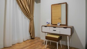 A small, neatly organized bedroom with a wooden vanity, a mirror, a bedside table, and a bench. - Modern 2BR Apartment at Maqna Residence (Jakarta)