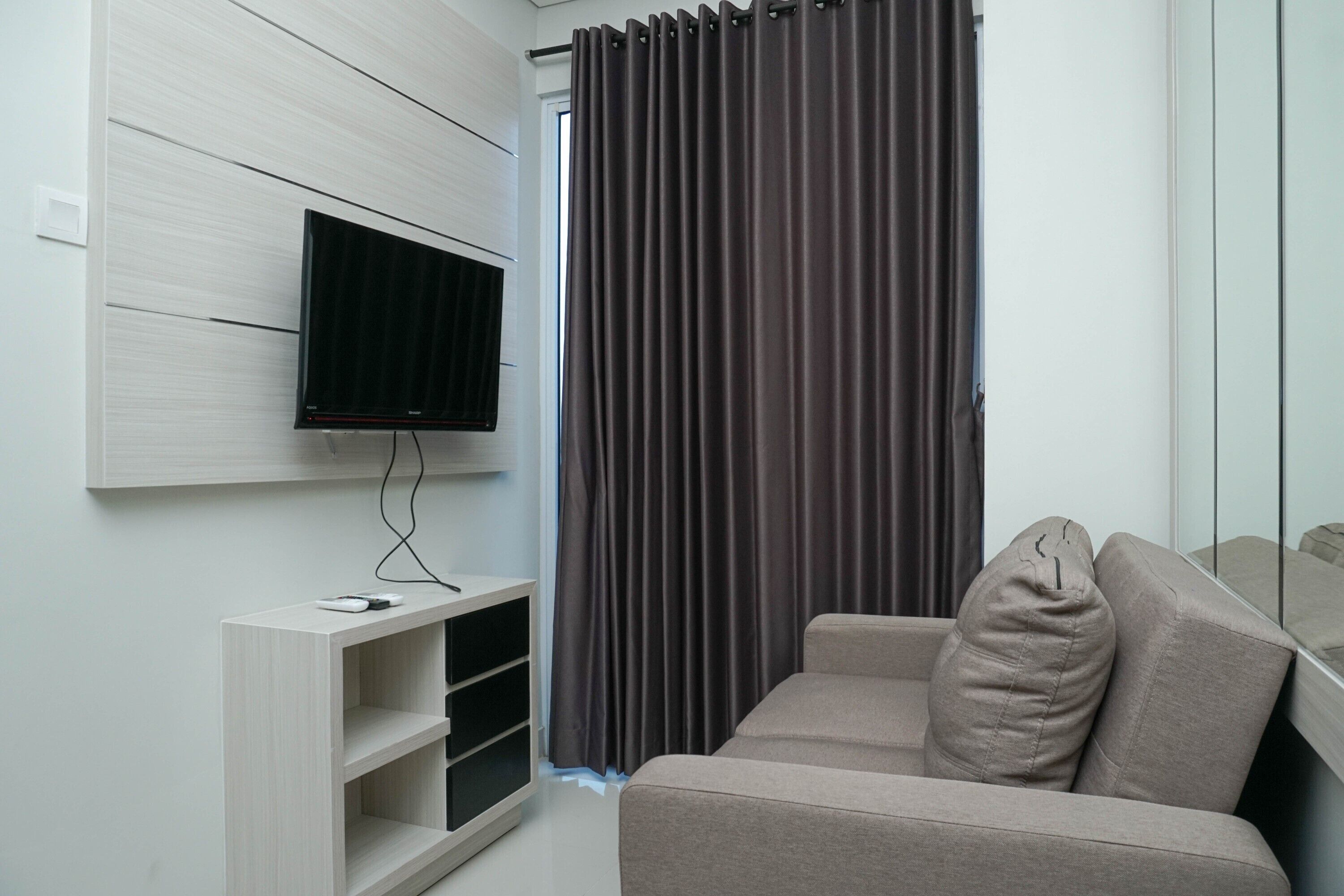Un salon moderne avec un téléviseur à écran plat fixé au mur, un canapé beige et un meuble de rangement en bois.