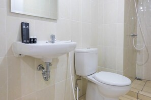 Un baño con lavamanos, inodoro y ducha blancos. Hay dos cepillos de dientes y un tubo de pasta de dientes sobre el lavamanos.