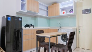 A compact kitchen with a refrigerator, washing machine, and a dining area with two chairs. - Best Price 2BR Apartment @ Midtown Residence (Gading Serpong)