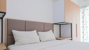 A modern bedroom with a large bed, two pillows, a wooden nightstand, and a built-in shelving unit. - Best Price 2BR Apartment @ Midtown Residence (Gading Serpong)