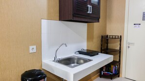 Une cuisine compacte dotée d’un évier en acier inoxydable, d’une bouilloire électrique noire et d’un meuble en bois placé au-dessus du plan de travail.