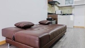 Una sala de estar moderna con un sofá de cuero marrón, una pequeña cocina con microondas y piso de madera.