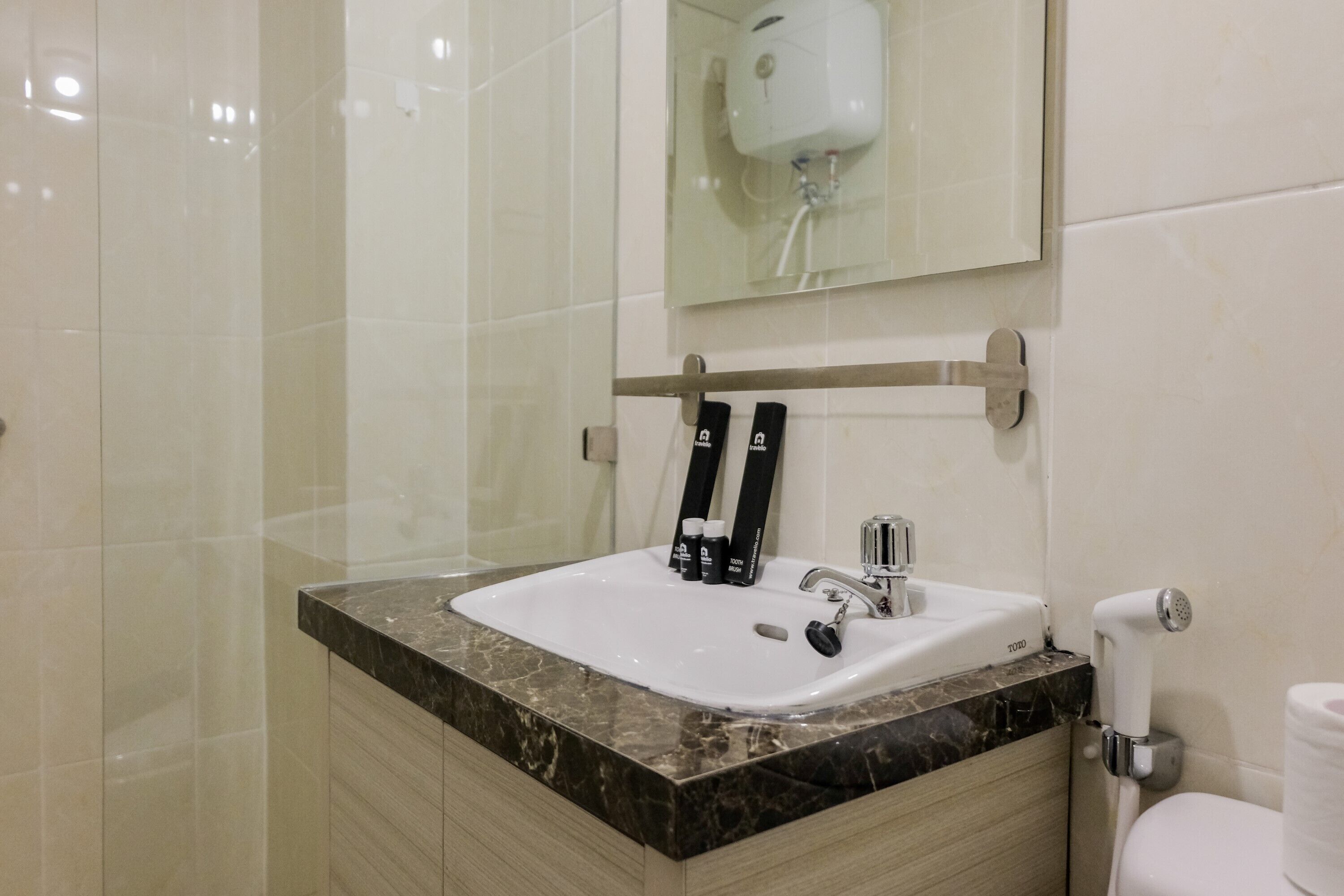 A bathroom with a white sink, a mirror, a towel dispenser, and a toilet.