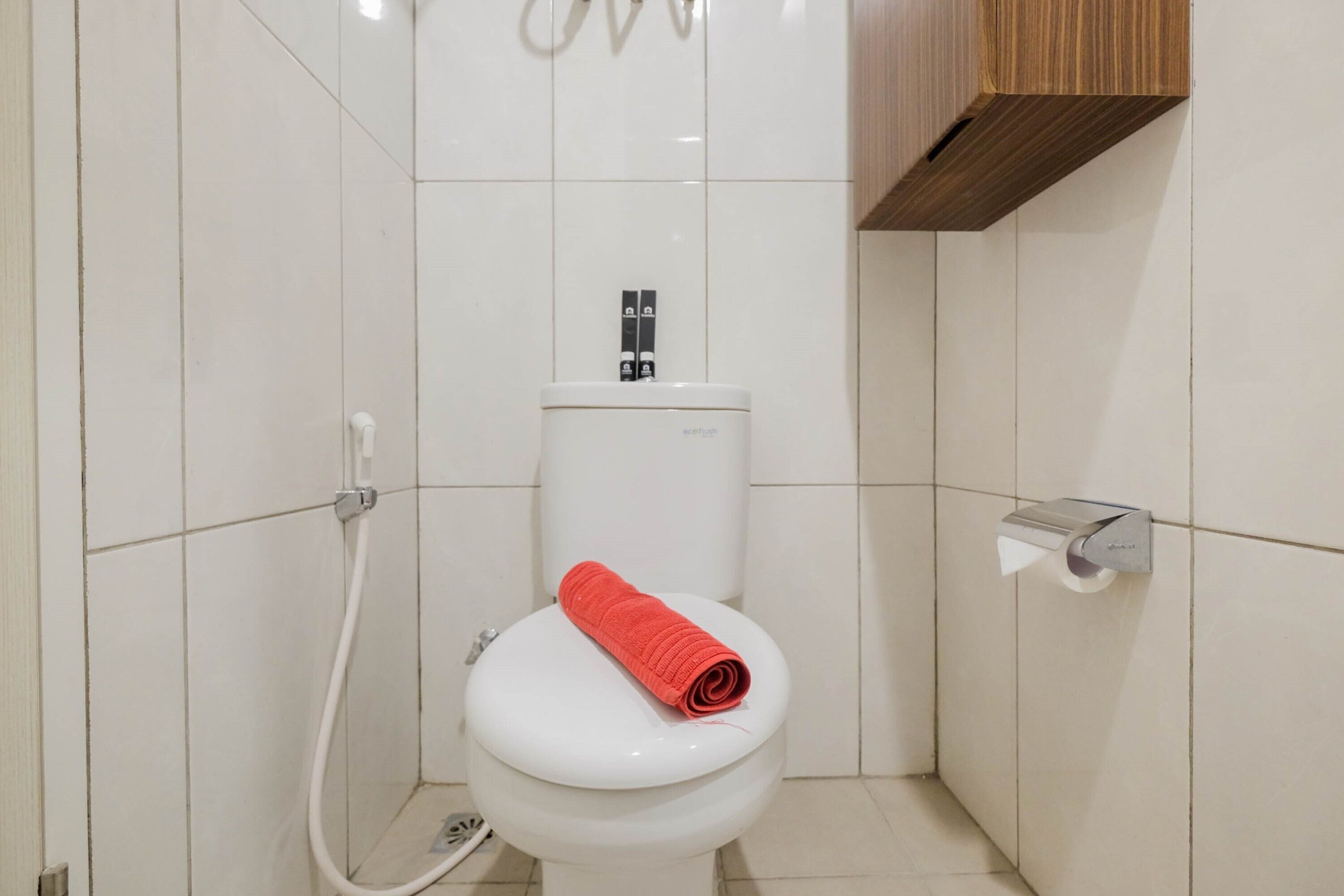 A bathroom with a white toilet, a shower hose, and a toilet paper holder.