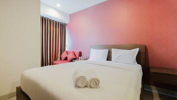 Una habitación de hotel con una cama, almohadas, una toalla enrollada, una silla roja y una cortina.