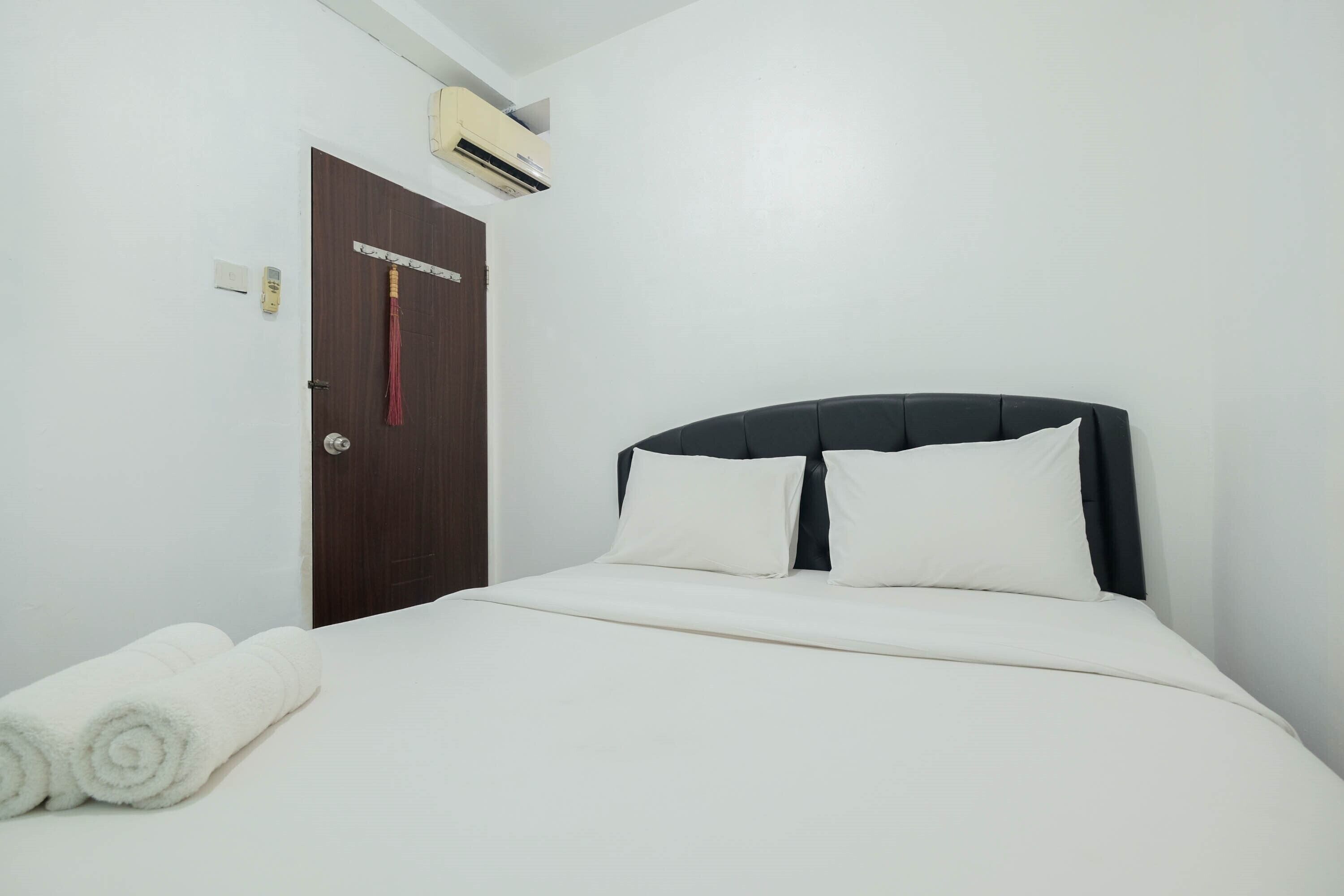 A neatly made bed with white linens and pillows, a dark headboard, and a white wall.
