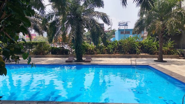 A swimming pool surrounded by lush greenery and palm trees. - New Furnished 2BR Apartment @ Mutiara Bekasi (Bekasi)