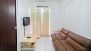 A small, modern living room with a brown leather sofa, a wooden coffee table, a flat-screen TV mounted on the wall, and a sliding door with vertical blinds. - New Furnished 2BR Apartment @ Mutiara Bekasi (Bekasi)