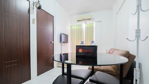 A room with a glass table, two black chairs, a brown sofa, a TV, an air conditioning unit, and a water dispenser. - New Furnished 2BR Apartment @ Mutiara Bekasi (Bekasi)