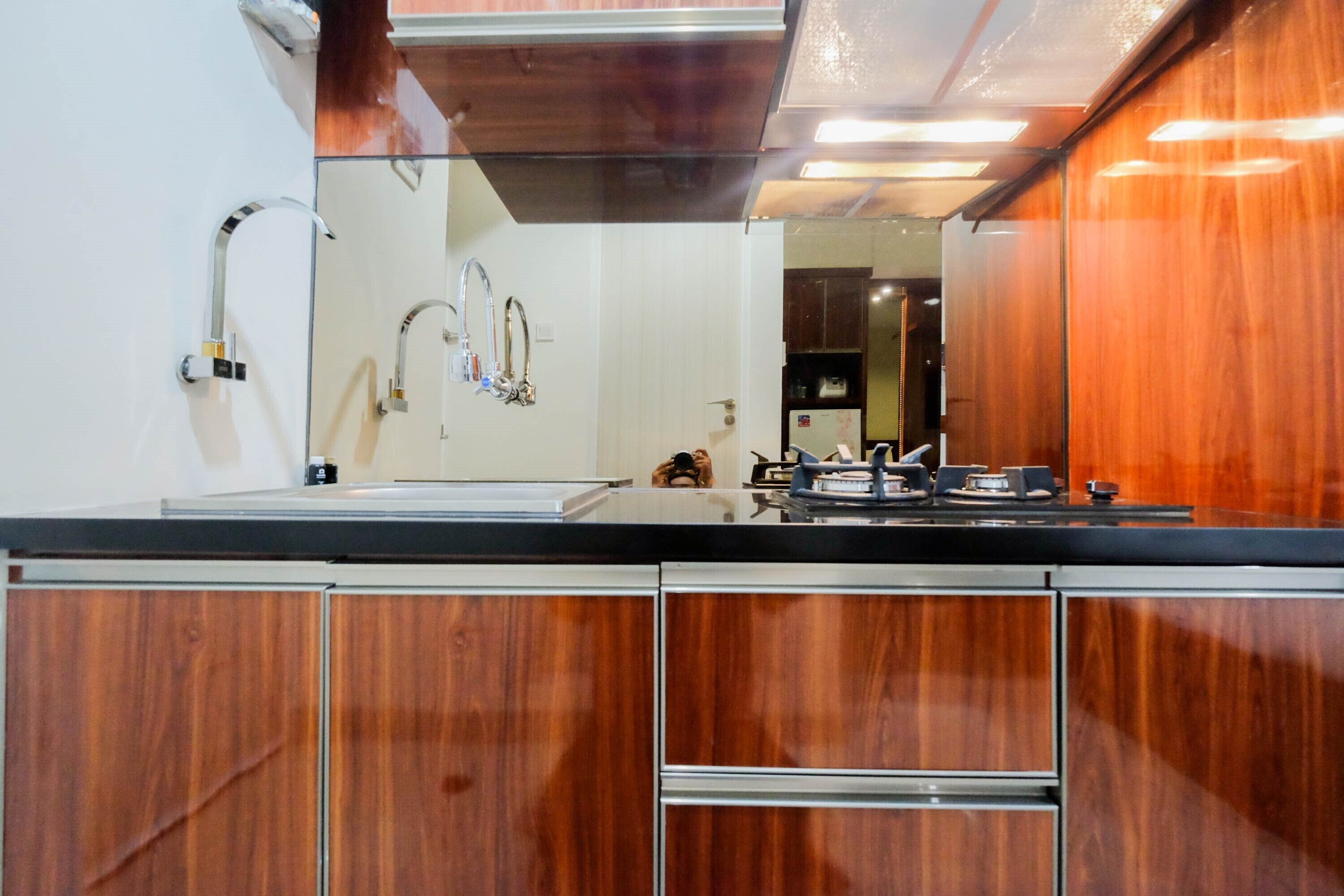 A modern kitchen with wooden cabinets, stainless steel appliances, and a large mirror above the countertop.