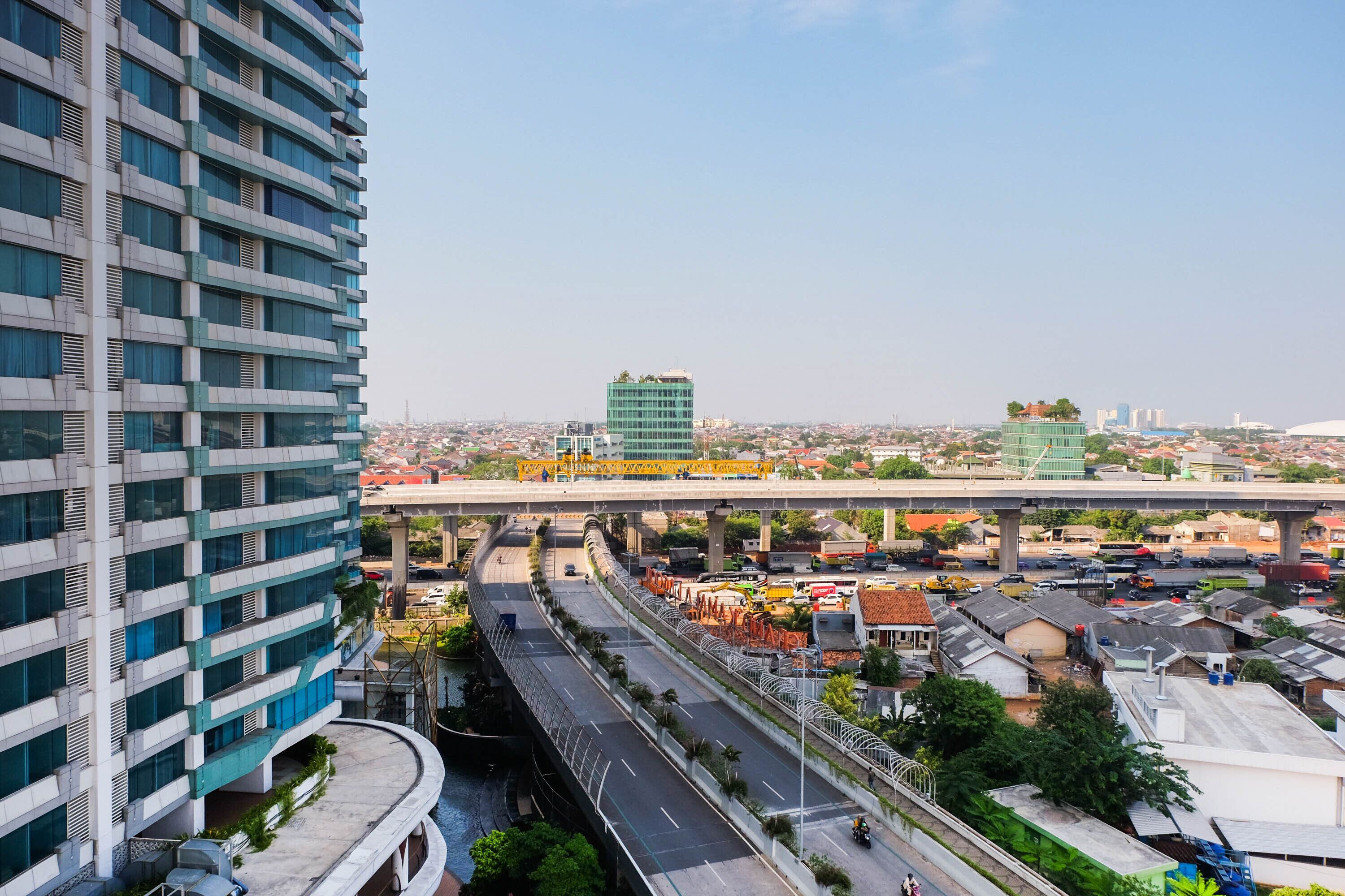 A multi-story building with a curved structure, an elevated roadway, and a distant view of a cityscape.