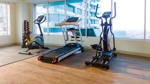 Un gimnasio con cintas de correr, elíptica y máquina de remo, amplias ventanas con vista a la ciudad.