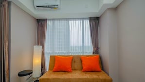 Une pièce comprenant un canapé, deux coussins orange, un lampadaire et un appareil de climatisation.