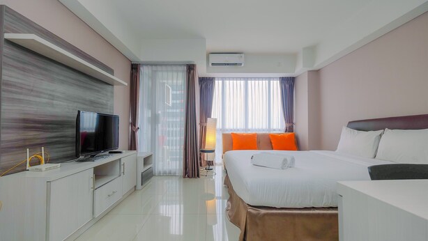Une chambre d’hôtel moderne dotée d’une télévision à écran plat, d’un lit avec une literie blanche et orange, d’une table de chevet et d’une grande fenêtre avec des rideaux.