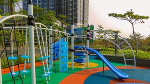 A playground with colorful play structures, including slides and climbing areas, surrounded by greenery and buildings.