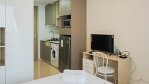 A compact hotel room with a bed, a desk with a TV, a washing machine, and a microwave.