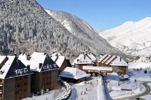 A snow-covered mountain resort with chalet-style buildings, a ski lift, and a clear view of the surrounding snowy landscape.
