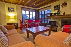 A cozy living room with a fireplace, wooden ceiling, and large windows. - Acebo - Val de Ruda - Two Bedroom Apartment, Sleeps 6 (Baqueira)