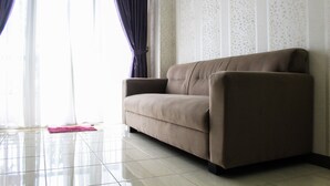A beige sofa in a room with a tiled floor and a patterned wall. - New Furnished 2BR Apartment at Silkwood Residence (Tangerang)
