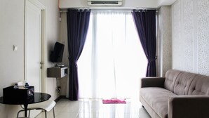 A living room with a sofa, a small table with a chair, a TV, and a window with curtains. - New Furnished 2BR Apartment at Silkwood Residence (Tangerang)
