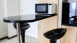 A kitchen with a microwave, a stove, and a black table with a stool. - New Furnished 2BR Apartment at Silkwood Residence (Tangerang)