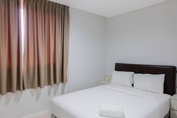 A hotel room with a single bed, white bedding, a dark headboard, and a nightstand with a lamp. - Luxurious and Comfy 2BR Paddington Heights Alam Sutera Apartment (Tangerang)
