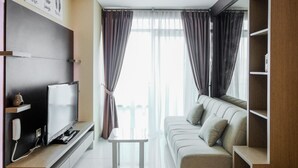 A modern living room with a flat-screen TV, a sofa, and a small table. - Best Price 2BR Apartment at Brooklyn Alam Sutera (South Tangerang)