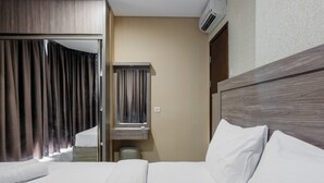 A hotel room with a bed, a mirror, a vanity, and a window with curtains. - Best Price 2BR Apartment at Brooklyn Alam Sutera (South Tangerang)