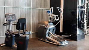 Two exercise machines in a gym with a mirrored wall and a weightlifting area in the background. - Cozy and Tidy 1BR Apartment at Brooklyn Alam Sutera (South Tangerang)
