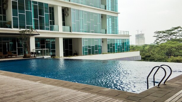 A modern building with a swimming pool, wooden deck, and glass windows. - Cozy and Tidy 1BR Apartment at Brooklyn Alam Sutera (South Tangerang)