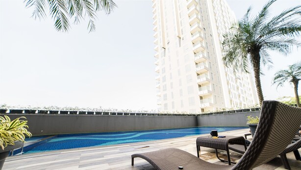 Zona de piscina en la azotea con sillones de descanso, una piscina y un edificio alto al fondo.