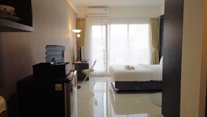 Habitación de hotel con cama, escritorio con dispensador de agua, lámpara y ventana grande con cortinas.