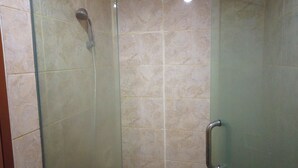 A glass-enclosed shower with a handheld showerhead, a tiled wall, and a metallic handle. - Unique Studio Galeri Ciumbuleuit Apartment near Dago (Bandung)