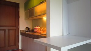 A kitchen with a wooden door, a countertop with a kettle, a pink container, and a white shelf. - Unique Studio Galeri Ciumbuleuit Apartment near Dago (Bandung)