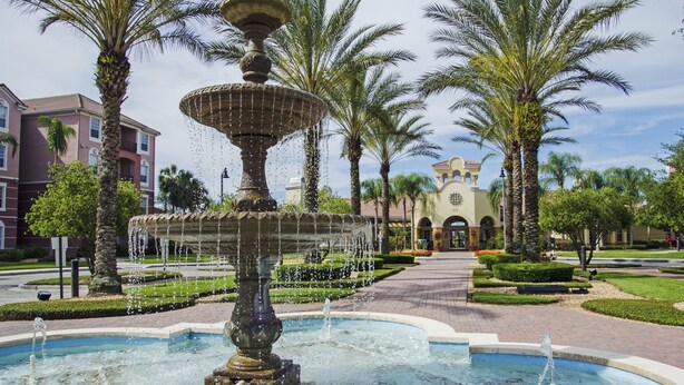 A fountain with multiple tiers and water jets, surrounded by palm trees and a well-maintained garden.