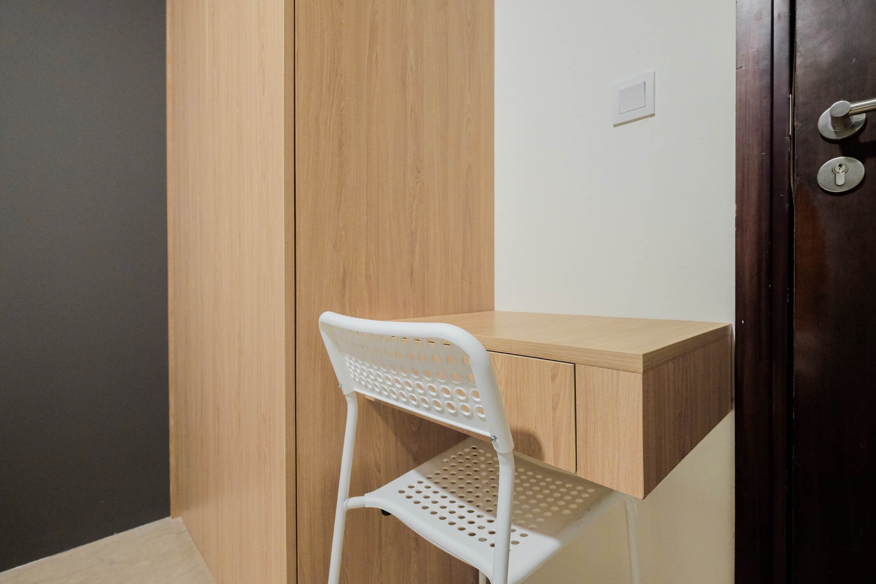 A white metal chair with a perforated backrest and seat, positioned in front of a wooden cabinet with a light-colored countertop.