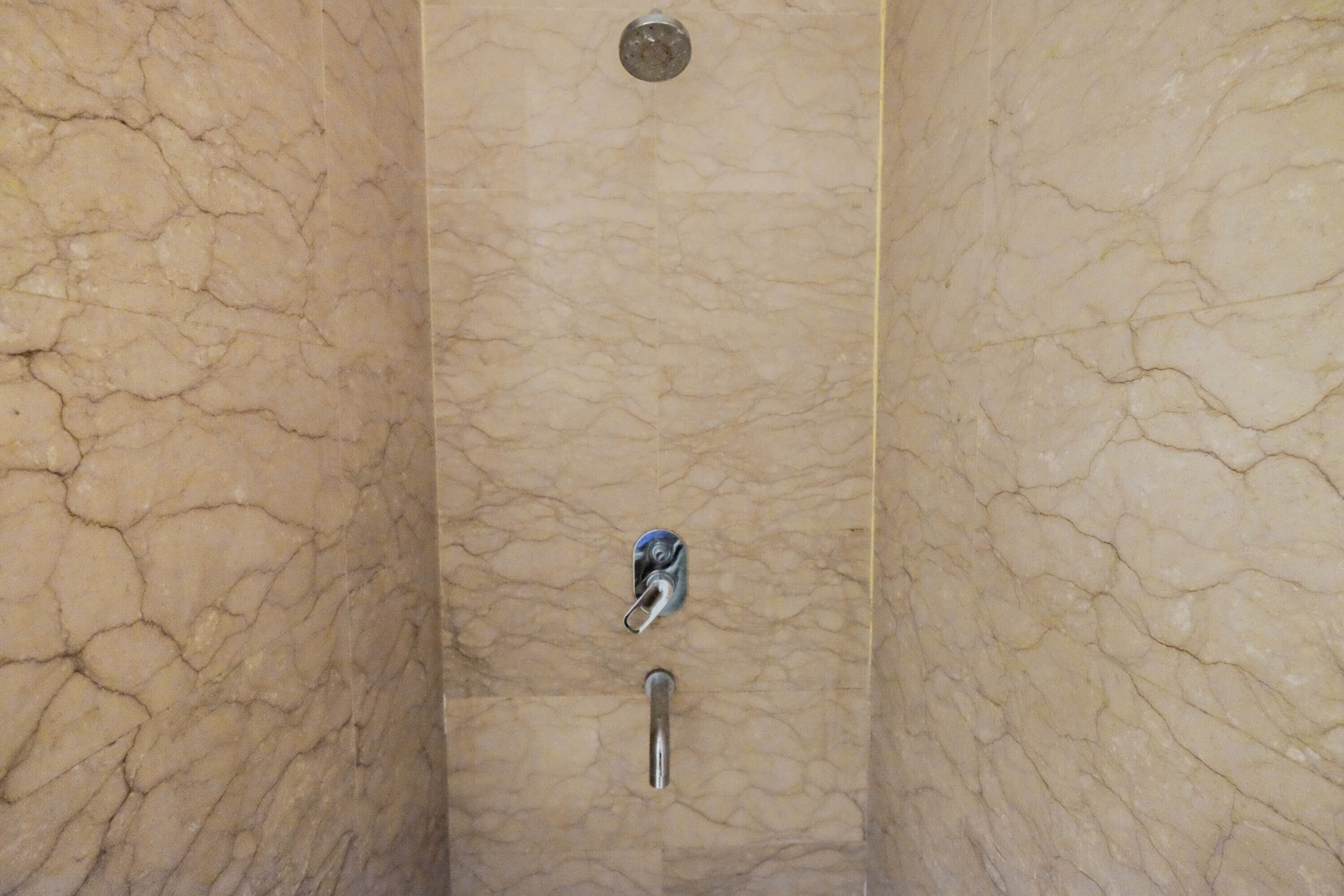 Un baño con pared de mármol, cabezal de ducha y grifo.