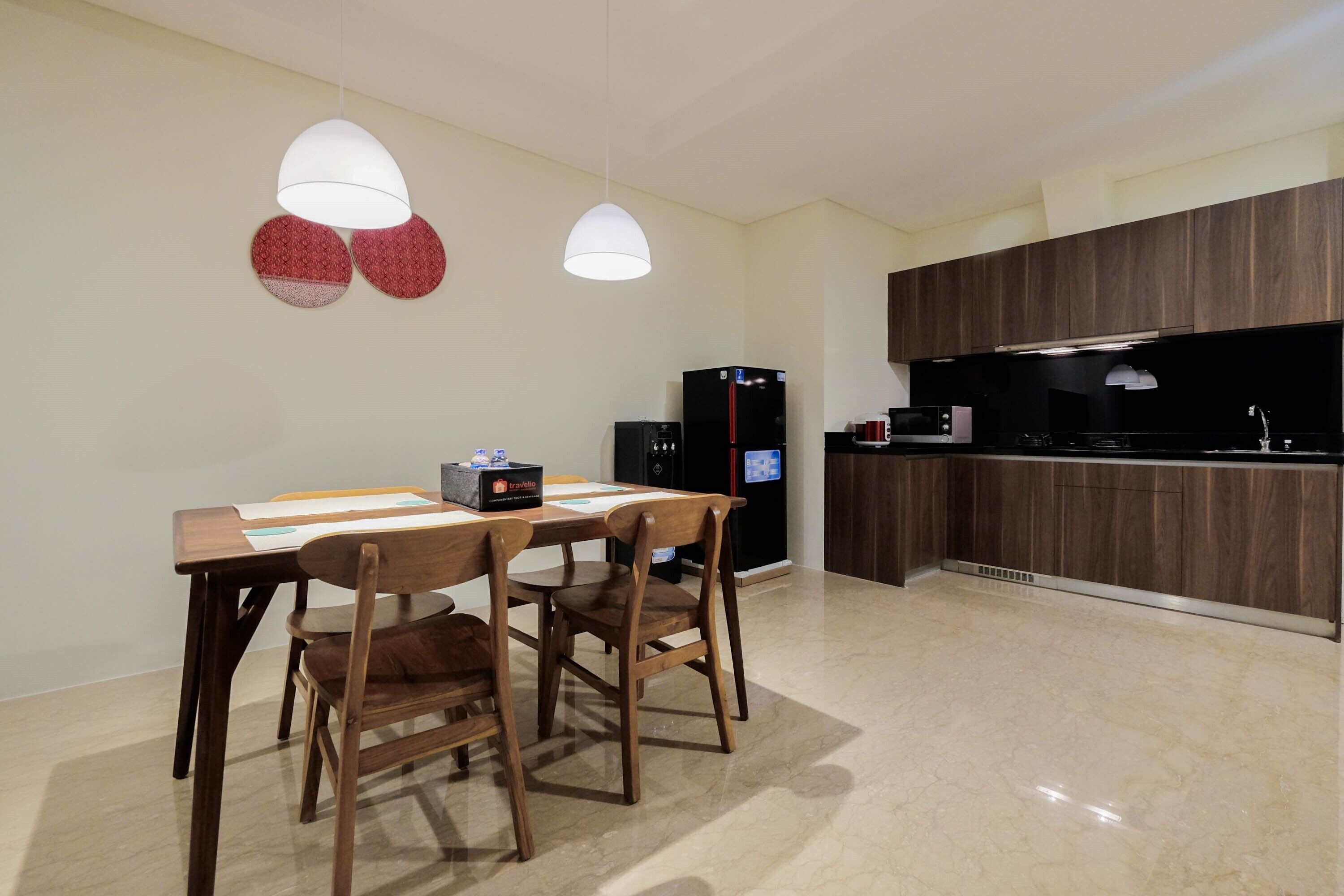 A modern kitchen with dark wood cabinets, a black refrigerator, and a microwave. There is a dining table with two chairs and a hanging light fixture above it.