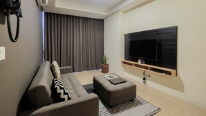 Ein modernes Wohnzimmer mit einer Couch, einem Hocker und einem Wand-Fernseher.