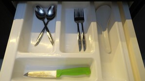 Un tiroir contenant un couteau à manche vert, une fourchette, une cuillère et une spatule.