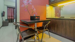 Une chambre d’hôtel dotée d’un coin repas comprenant une table et deux chaises en osier, un petit sac noir posé sur la table, et un mur décoratif orné d’une fresque florale.