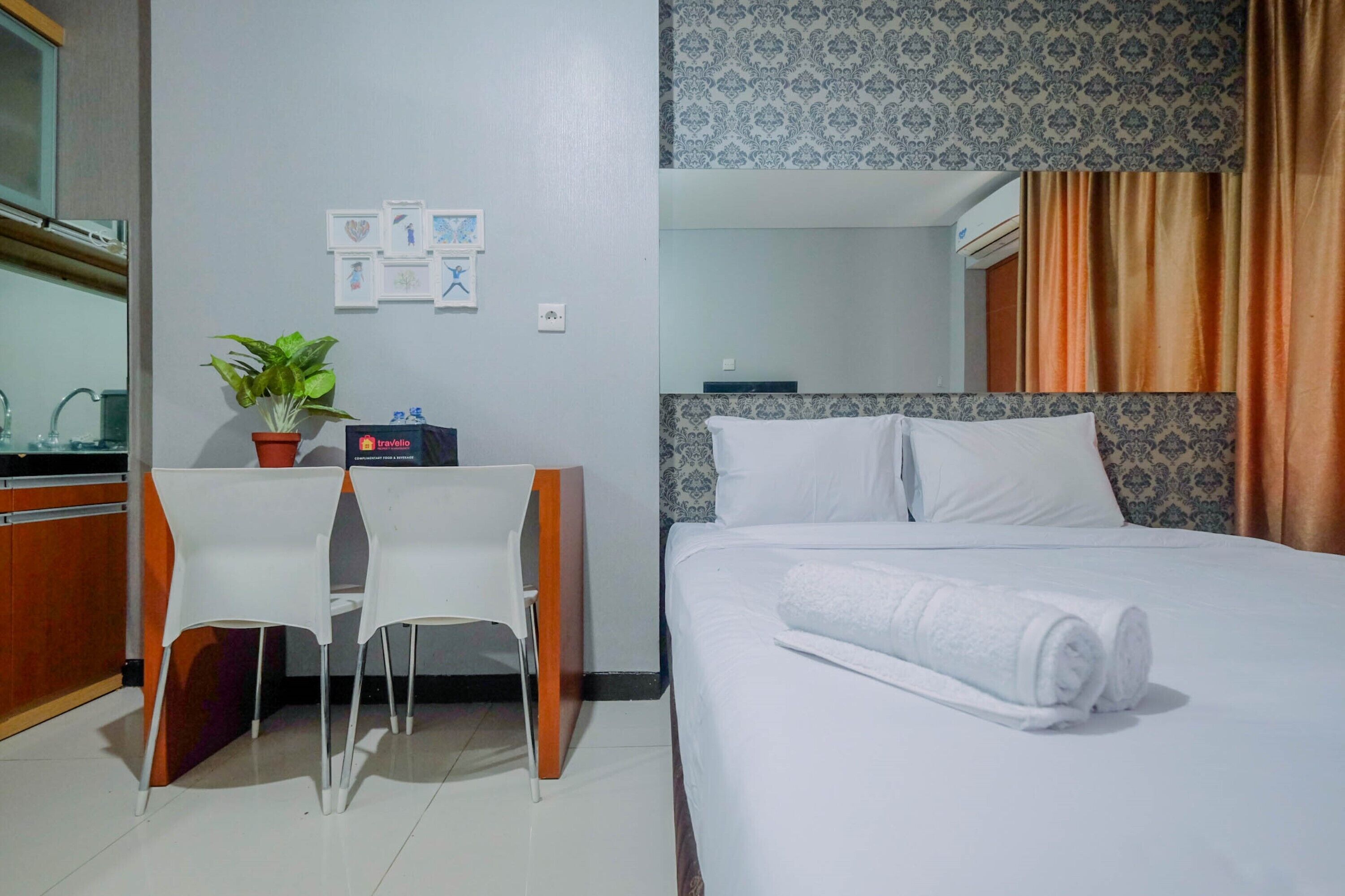 Habitación de hotel con una cama, un escritorio con una silla, una planta en maceta y una pequeña mesa.